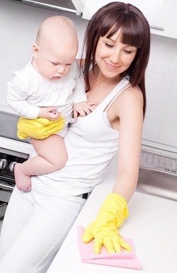 Няня с младенцем на руках делает уборку на кухне